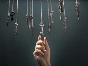 A hand reaching up to select one specific key among many hanging from strings, representing the use of intuition in decision making.
