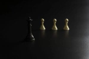 A black queen chess piece standing in front of three white pawn pieces on a dark background, illustrating the concept of responsible leadership.