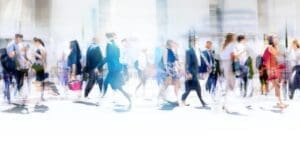 A blurred motion shot of a busy crowd in a bright urban space, representing how great companies think differently amidst the noise.
