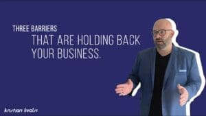 Kristian Livolsi gesturing with open hands against a blue background, presenting three common business barriers that are holding back your business.