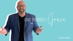 Kristian Livolsi gesturing with open hands against a light blue background, illustrating the importance of learning to give yourself grace in business and life.