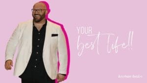 Kristian Livolsi smiling in a white blazer against a pink background, illustrating the mindset needed to live your best life.